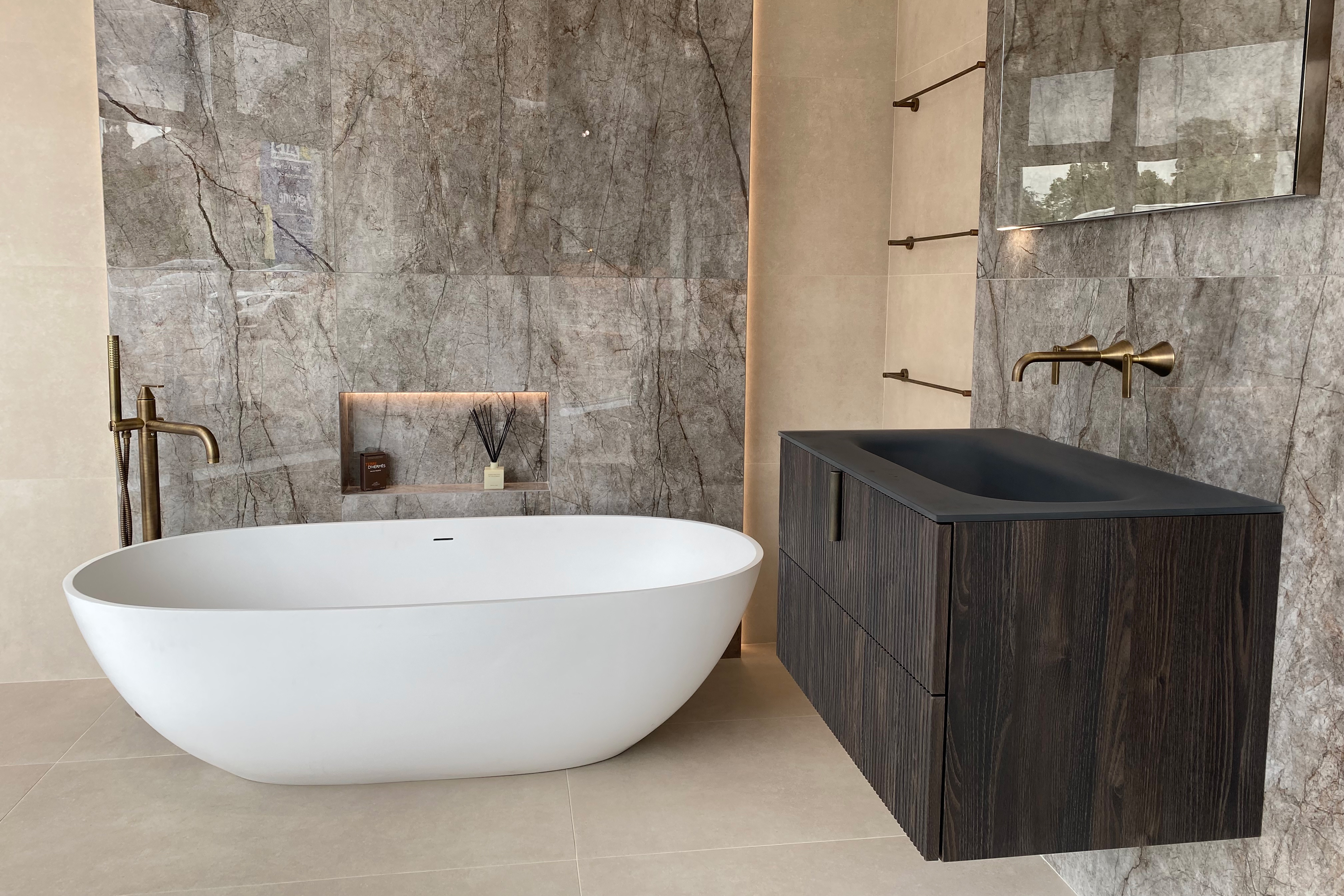 A modern bathroom with large freestanding white bathtub, wood panelled vanity and large mirror.